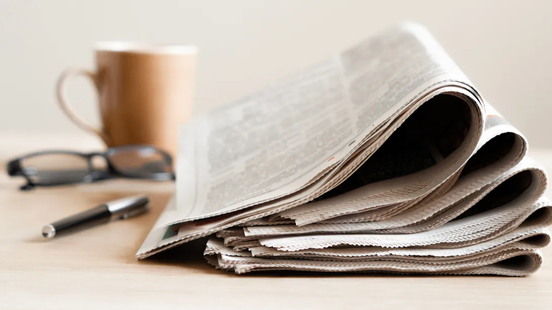 Newspapers in the process of being read with coffee mug, spectacles and pen in background